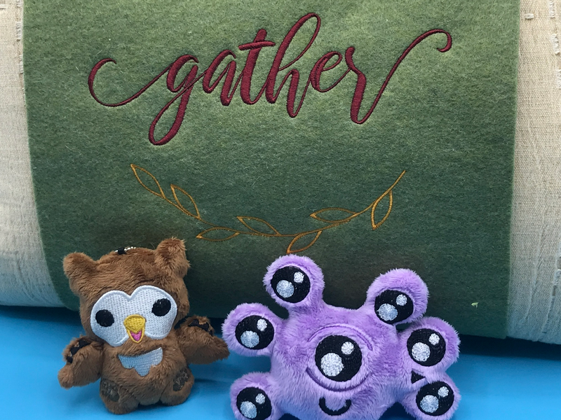 Tiny plush owlbear and beholder charms next to a very wedding-script pillow wrap.