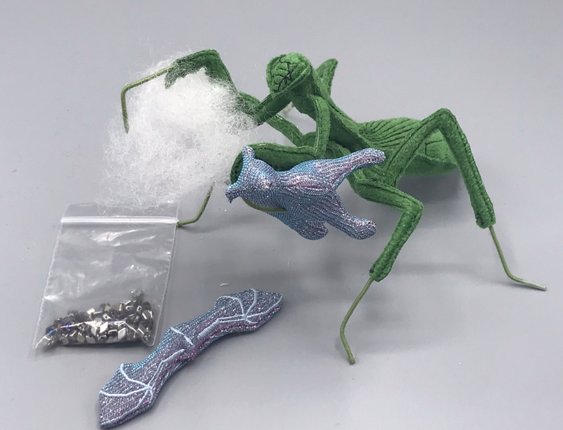 A velvet Carolina mantis with a plush dragon in one claw and a clump of stuffing in the other