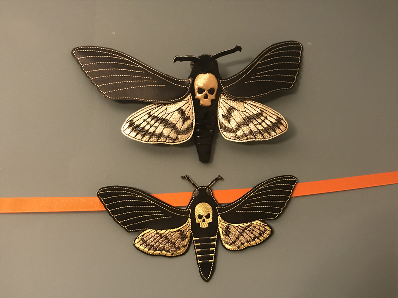 Two mostly-faux-leather moths on the wall: one a plush body with faux-leather wings, the other a single-piece faux-leather.