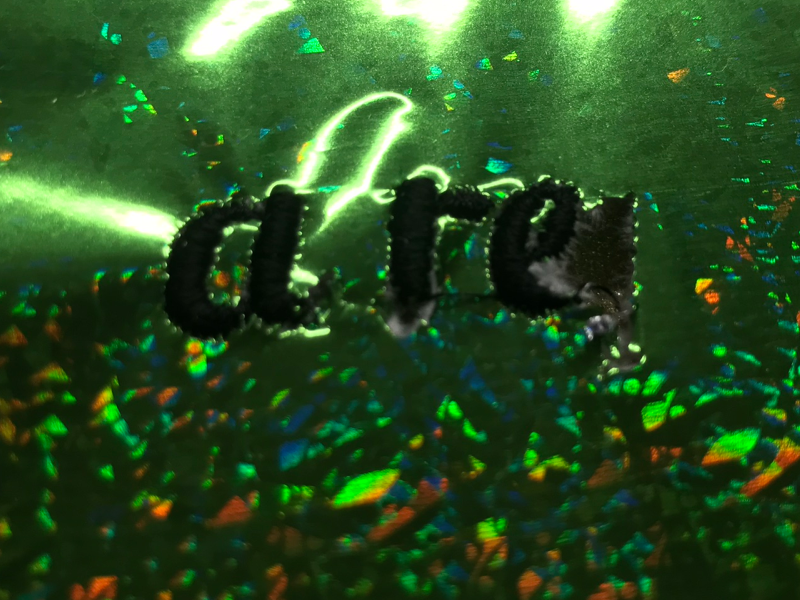 Shattered-glass hologram in green, with letter-shaped holes stitched into it