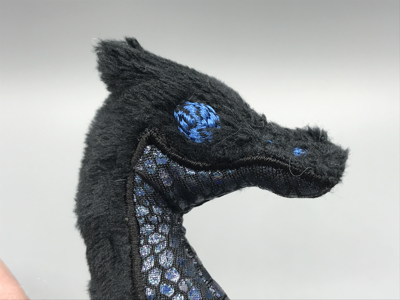 A tiny plush dragon. Its eye and nostril are machine embroidered, albeit just a basic test shape, and its underside is appliqued iridescent fabric.