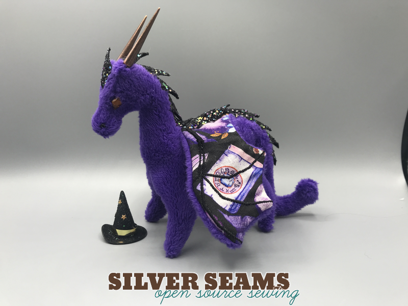 A tiny plush dragon with a tiny witch hat next to it.