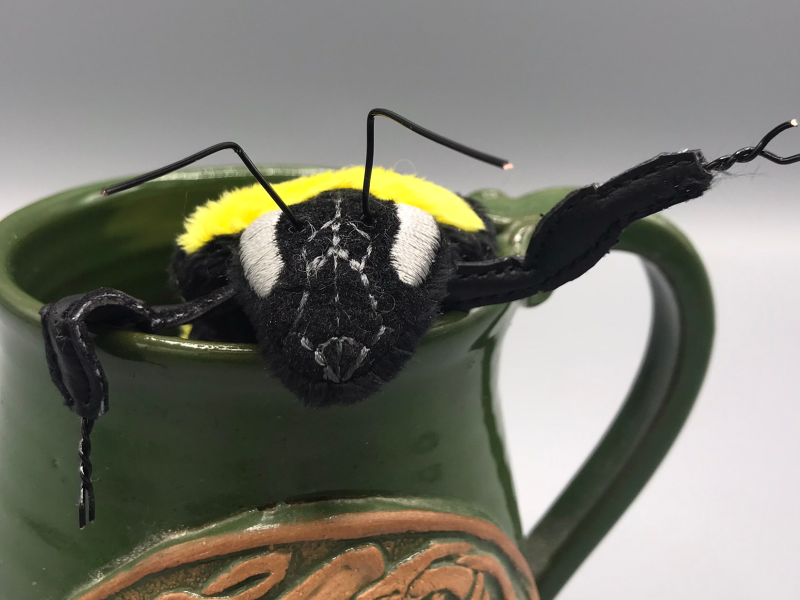 A plush bee, waving from inside the dragon mug prop.