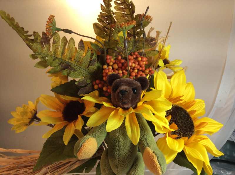 Teddy bear with flower ruff in front of flower arrangement