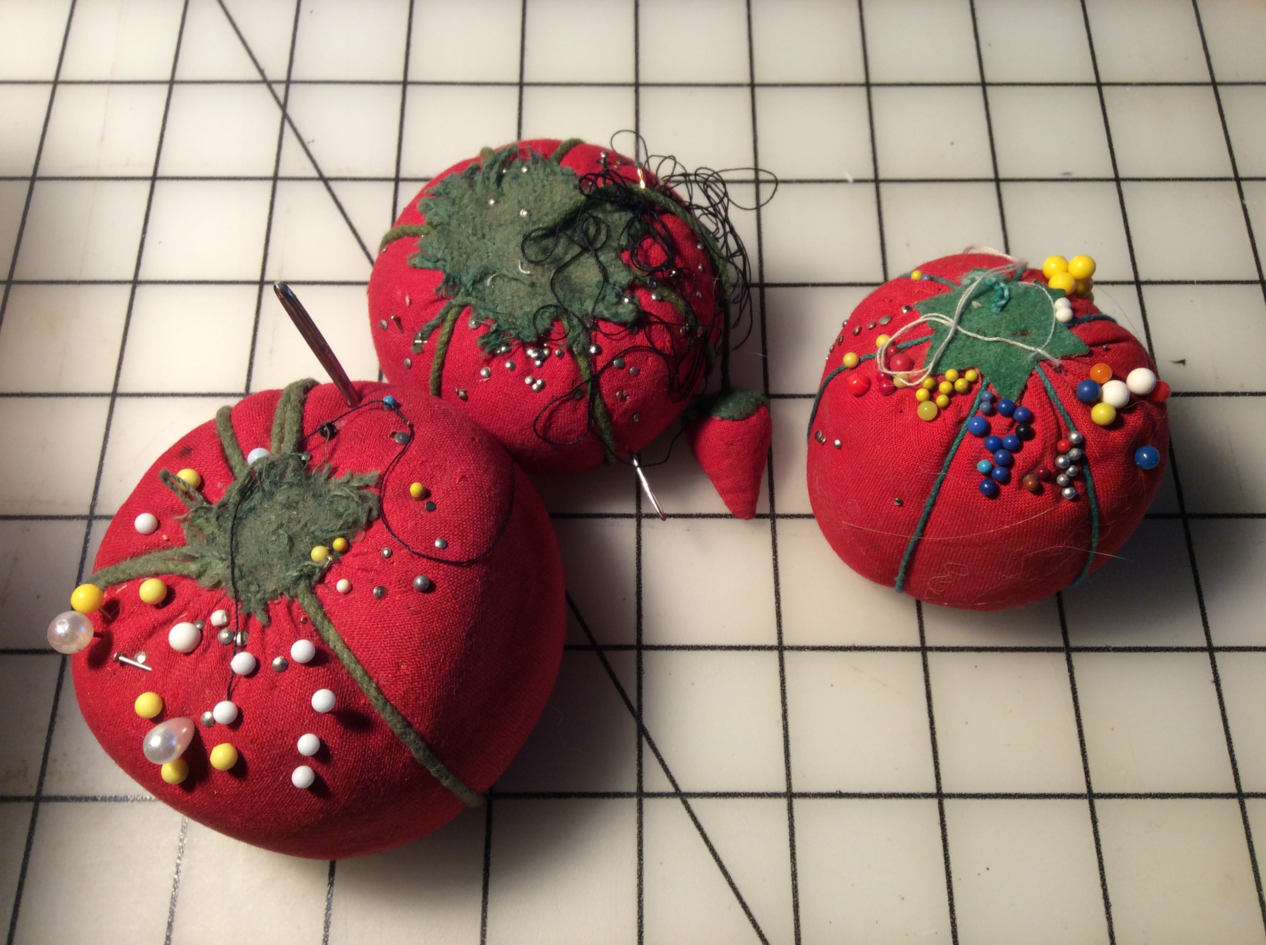 Three tomato-shaped pincushions, one with an attached "strawberry."