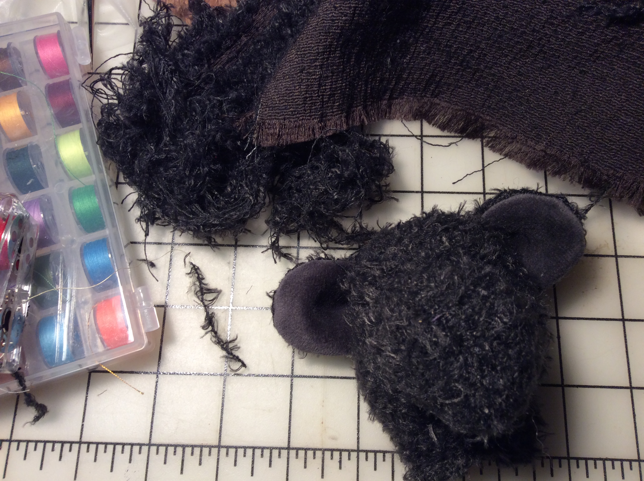 A black, unfinished teddy bear head next to a snarl of yarn as big as it is.